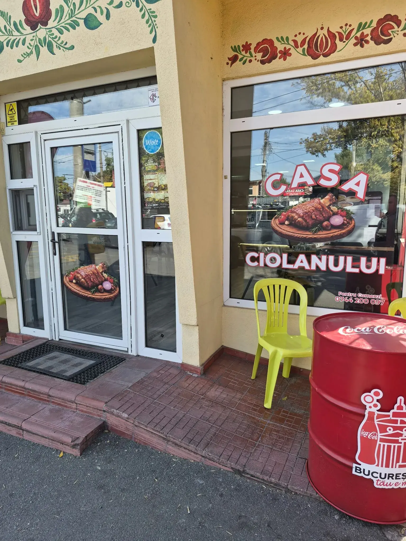 Fațada Casei Ciolanului, cu geamul decorat, motive florale pictate și butoiul roșu de la intrare